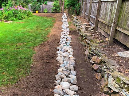 Drainage Set Up With Rocks In A Backyard Along A Fence