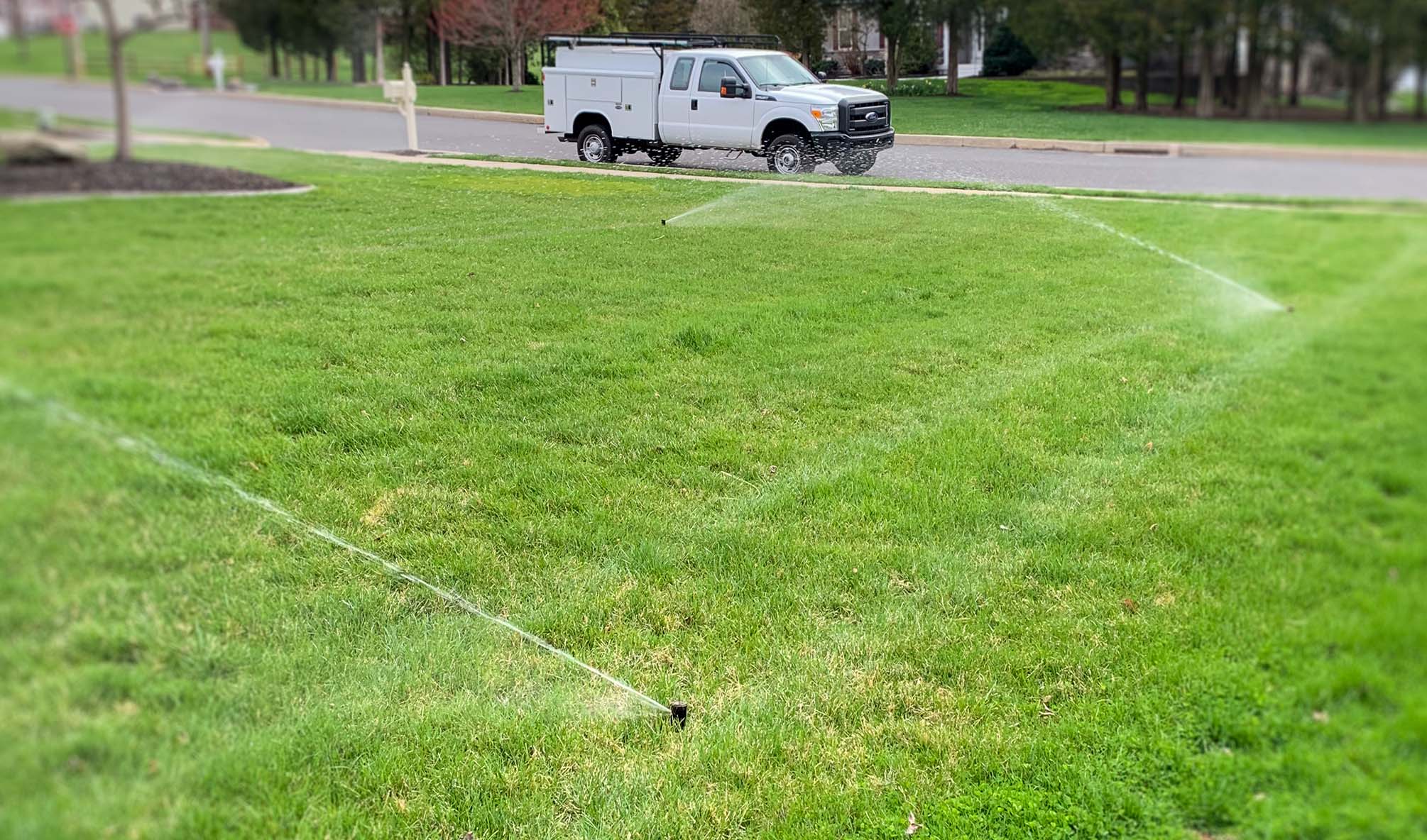 Sprinkler Irrigation Turned On In A Yard With A Truck Parked Out Front