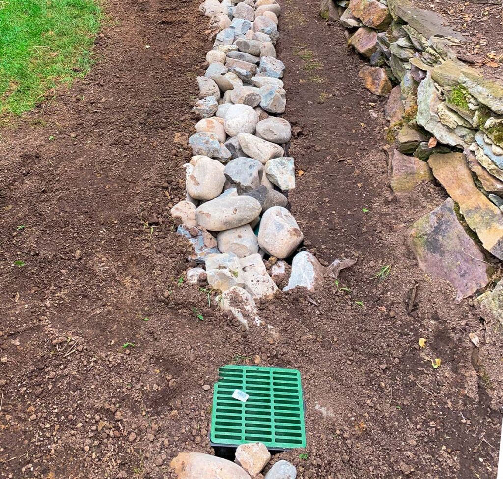 Drainage Set Up With Rocks In A Backyard Along A Fence