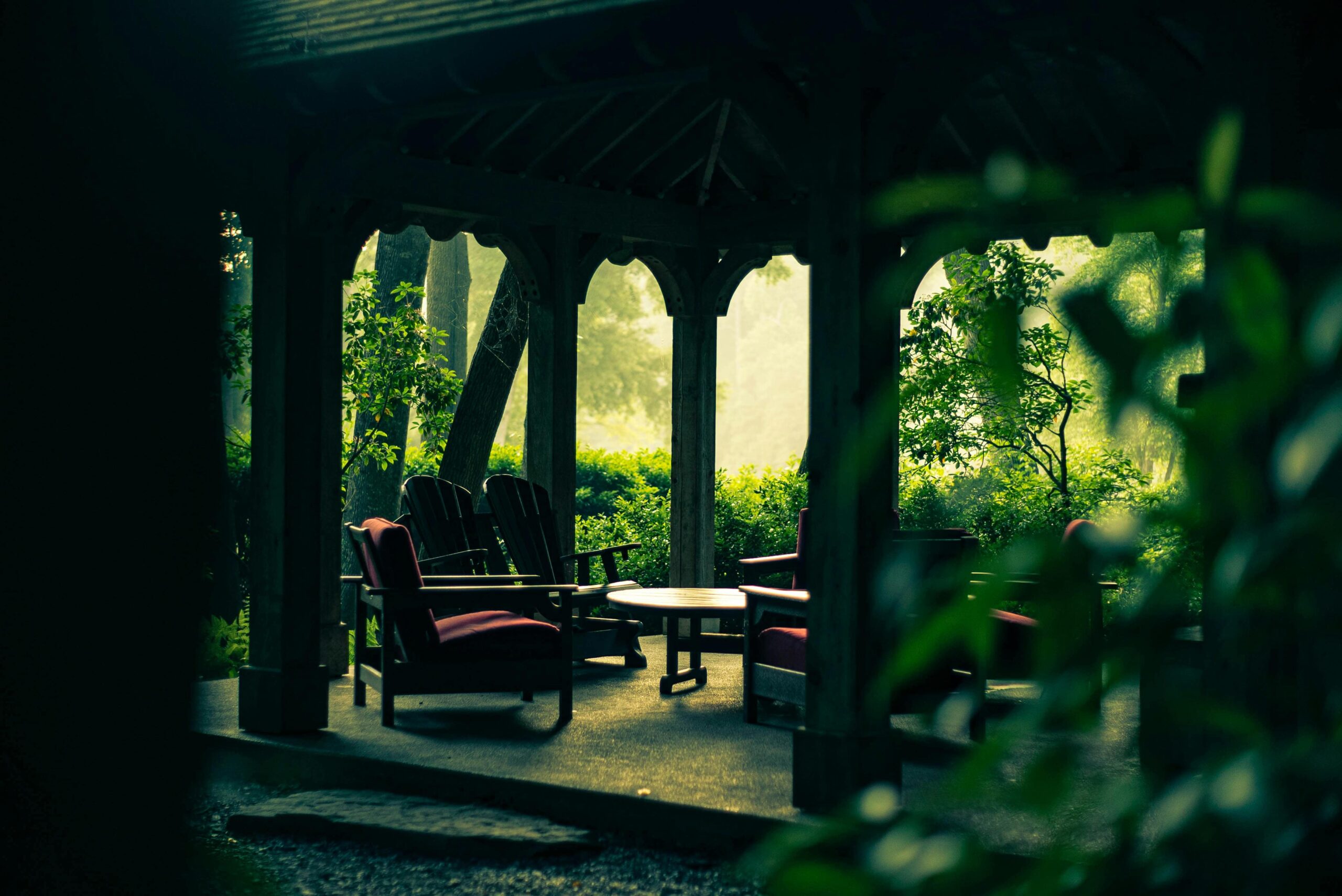 A shaded wooden gazebo surrounded by dense greenery, offering a tranquil retreat.
